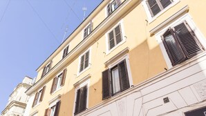 A multi-story building with a yellow facade, white trim, and a large wooden door at the ground level. - St. Peter Beautiful 2BR Apartment (Roma)