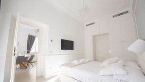 A bedroom with a large bed, a flat-screen TV mounted on the wall, and a dining area with a table and chairs. - St. Peter Beautiful 2BR Apartment (Roma)