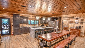 A spacious kitchen with a large island, dark wooden cabinets, and a rustic ceiling. - Fox Trot Lodge - 6 King Suites - Pickleball Court (Broken Bow)