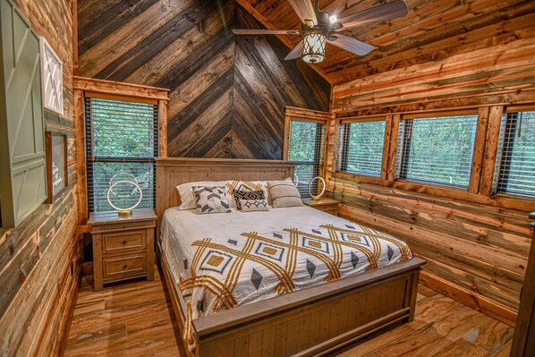 Un dormitorio de cabaña de madera con una cama, mesitas de noche y un ventilador de techo.