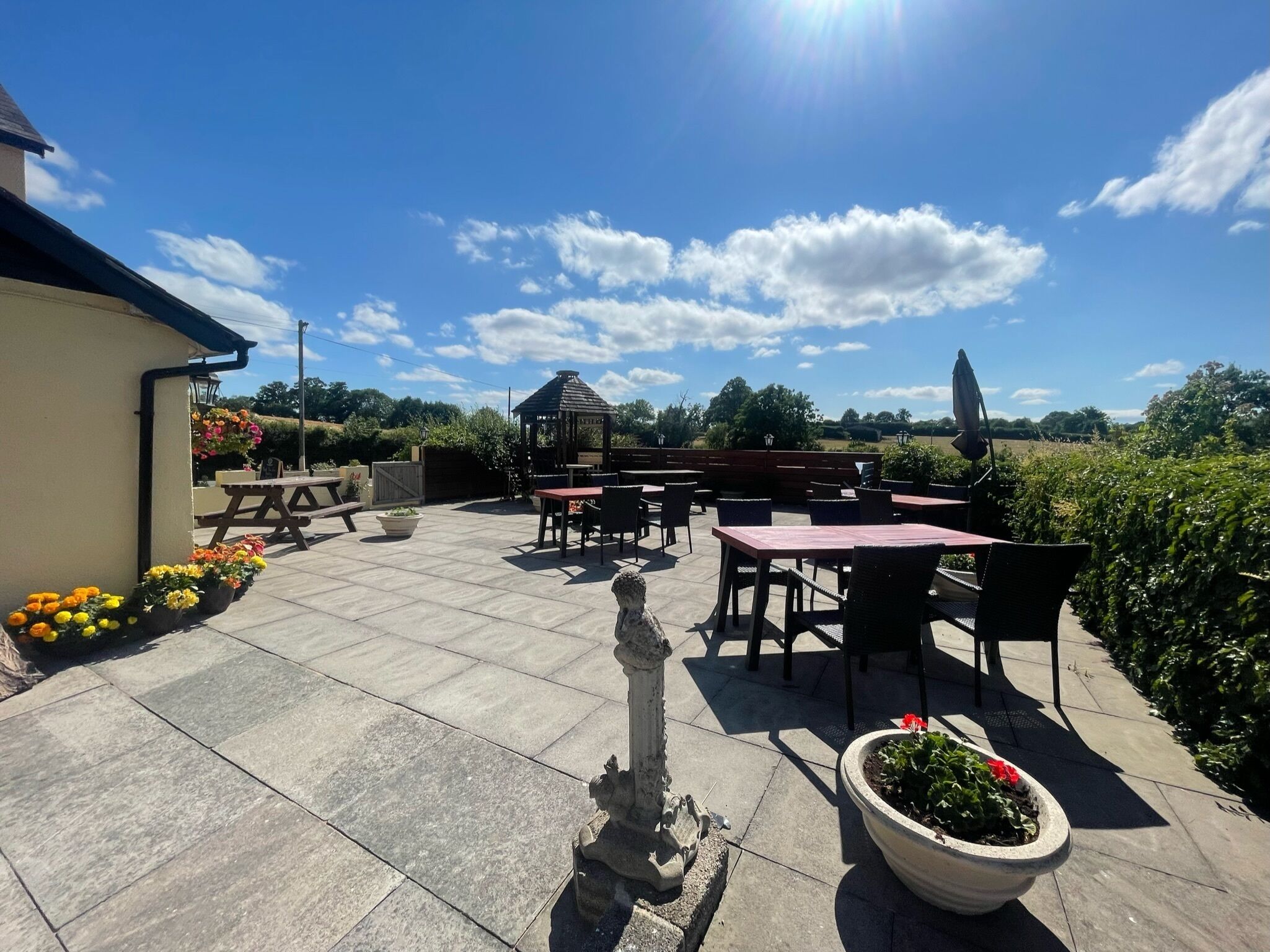 An outdoor patio with stone flooring, multiple tables and chairs, a gazebo, and potted plants.