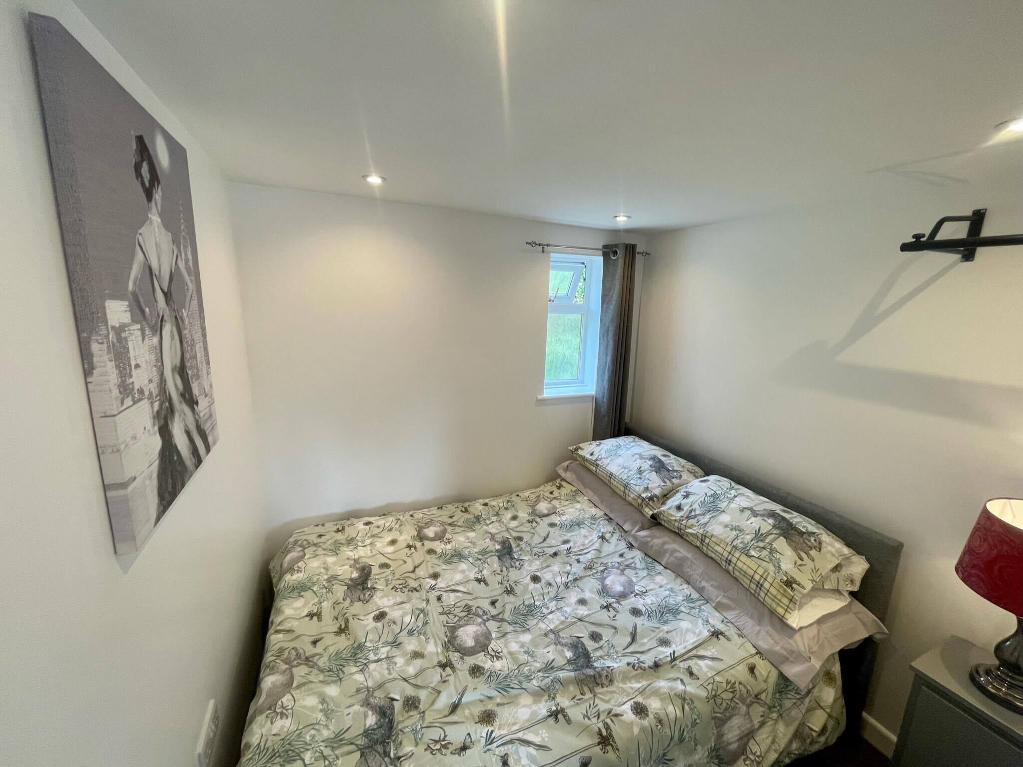 A bedroom with a bed, a window, a wall-mounted lamp, and a poster.