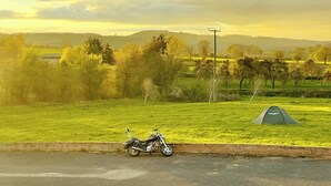 A motorcycle parked beside a road with a tent in a grassy field.