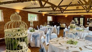 A banquet hall with round tables set for a formal event, featuring white tablecloths and blue sashes on chairs.