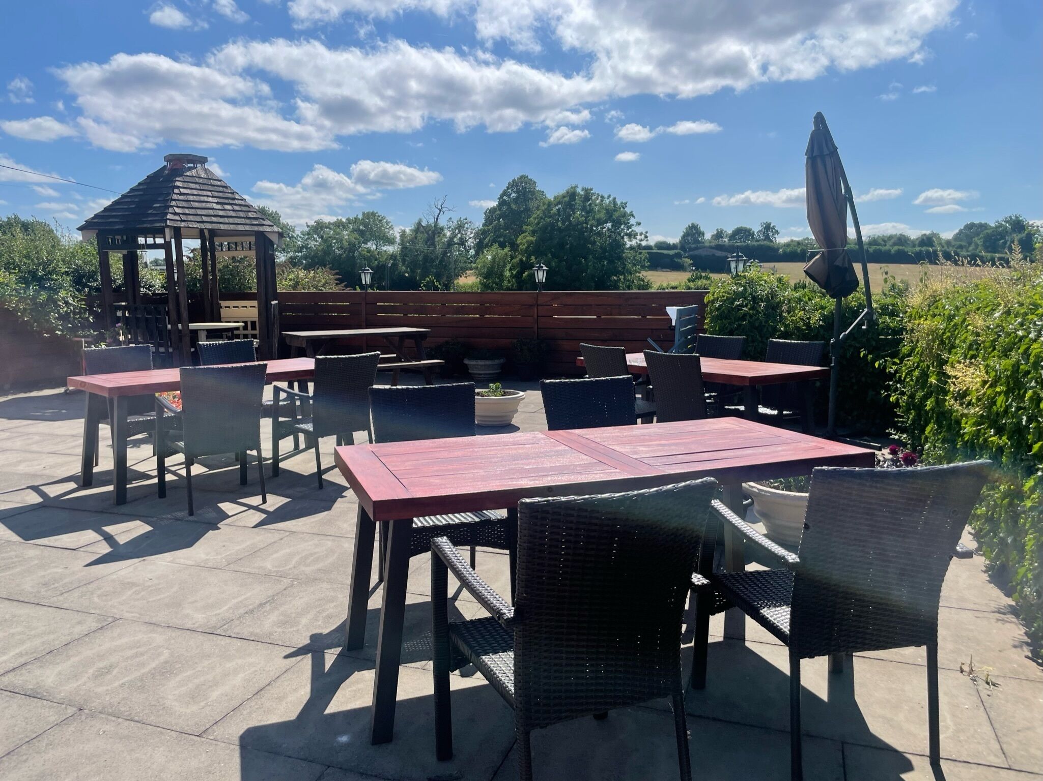Une terrasse extérieure dotée de plusieurs tables et chaises, d’un belvédère en bois et offrant une vue sur la verdure environnante.