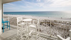 Ein Balkon mit weißen Stühlen und einem Tisch mit Blick auf einen Strand und das Meer.