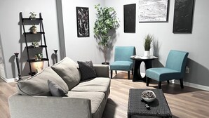 A modern living room with a grey sofa, teal armchairs, a coffee table, a black bookshelf, and a potted plant. - Central Madison Spot Near Work & Attractions (Madison)