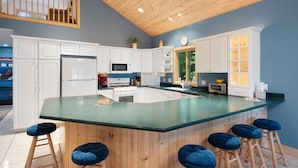 Una cucina moderna con mobili bianchi, una grande isola con sgabelli, un soffitto in legno e vista sul verde.