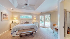 A bedroom with a bed, bedside tables, a ceiling fan, a window, and a view of the outdoors.