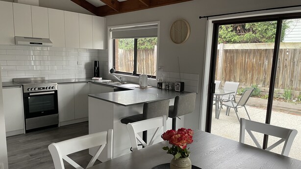 Une cuisine moderne avec des meubles blancs, un four encastré et un coin repas comprenant une table et des chaises.