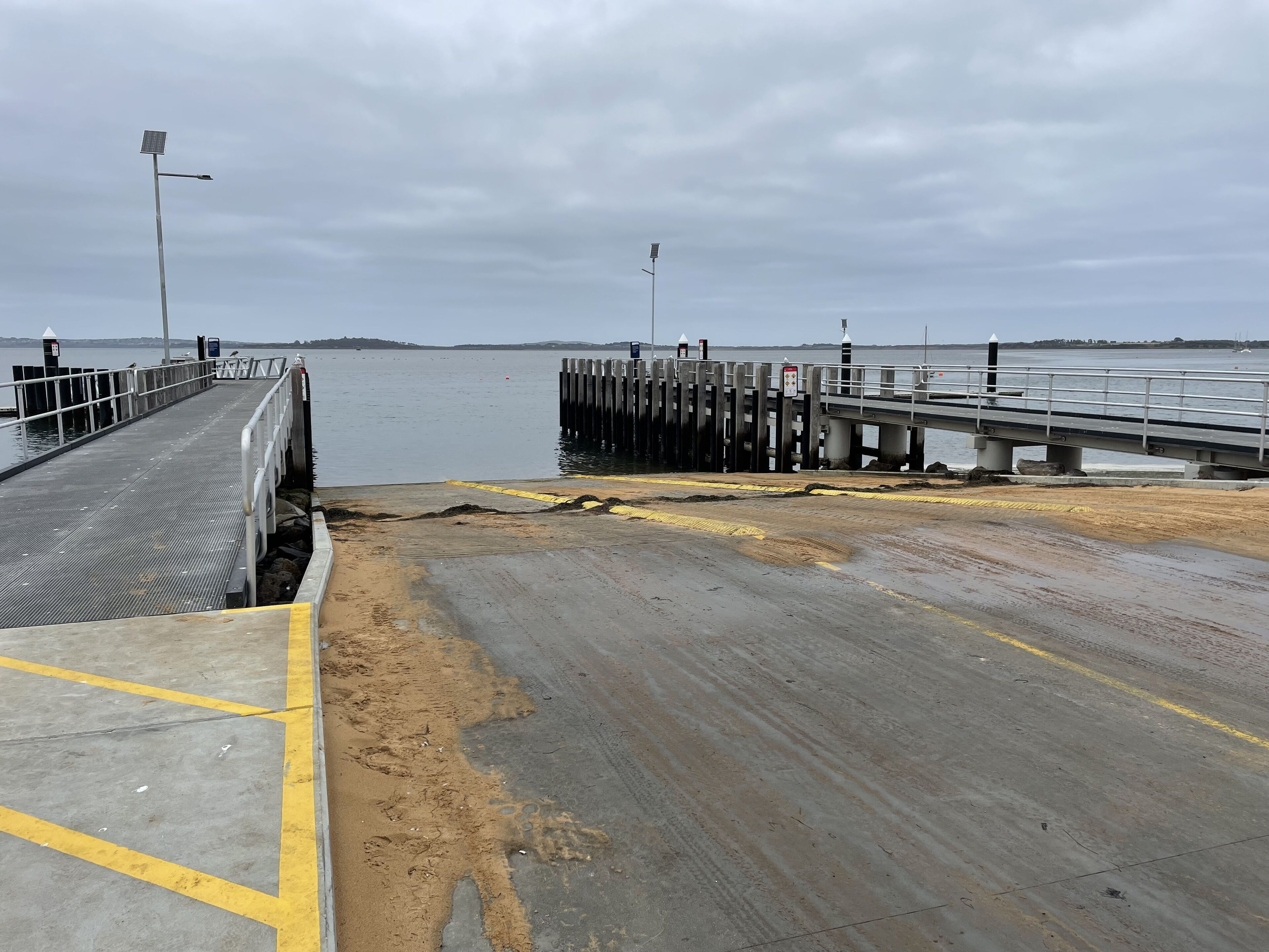 A pier extending into calm water with a sandy area at the end.