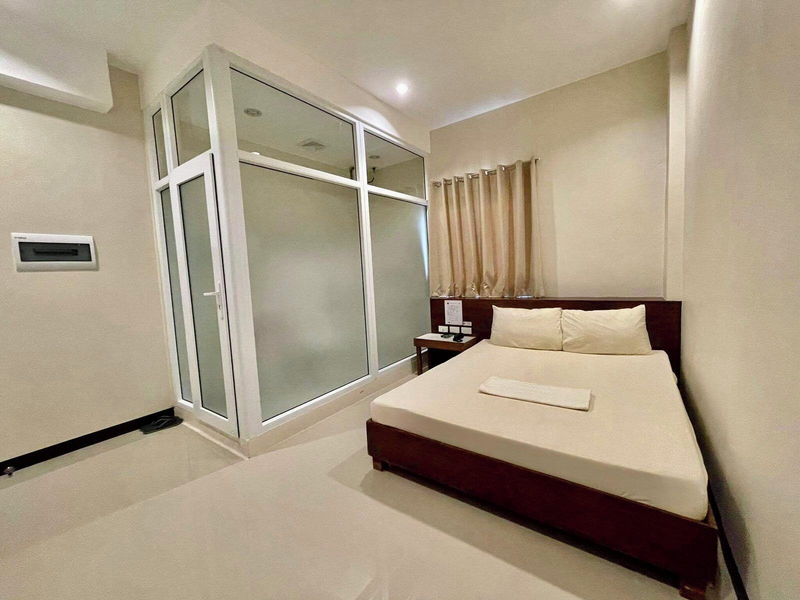 A modern hotel room with a large bed, a sliding glass door, a nightstand, and a window with curtains.