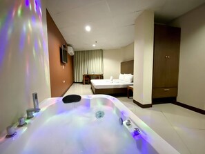 A hotel room with a large bathtub, a bed, a desk, and a wardrobe. - ASIATEL Bacoor (Bacoor City)