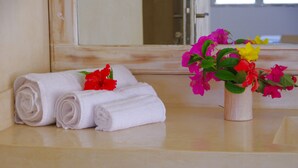 A neatly folded white towel and a vase with pink and yellow flowers on a bathroom counter.