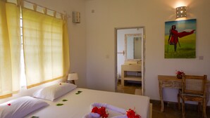 A hotel room with a bed, a desk, a chair, a painting, and a bathroom visible through an open door.
