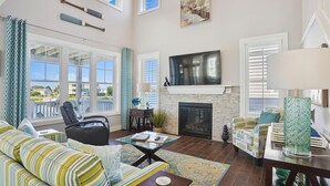 A spacious living room with a sofa, a coffee table, a fireplace, and a TV mounted above it. - CH219C- Beautiful Canal front - Kill Devil Hills - Saturday Check In! (Kill Devil Hills)