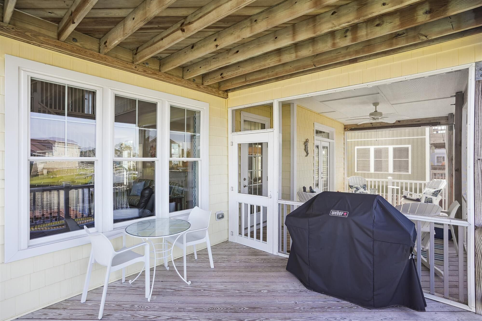 A covered outdoor patio with a grill, white chairs, and a glass table.