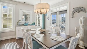 A dining area with a wooden table, white chairs, and a chandelier. - CH219C- Beautiful Canal front - Kill Devil Hills - Saturday Check In! (Kill Devil Hills)