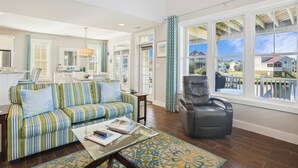 A spacious living room with a striped sofa, a leather chair, and a glass coffee table. - CH219C- Beautiful Canal front - Kill Devil Hills - Saturday Check In! (Kill Devil Hills)