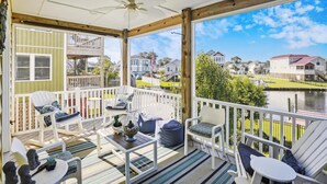 A covered porch with white railings, multiple seating areas, and a view of a residential area and water body. - CH219C- Beautiful Canal front - Kill Devil Hills - Saturday Check In! (Kill Devil Hills)