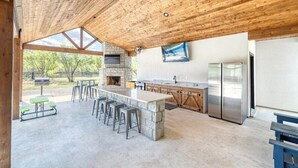 A spacious outdoor kitchen with a stone island, bar stools, and a stone fireplace. - River Ridge @ Frio Premier Rental Homes (Concan)