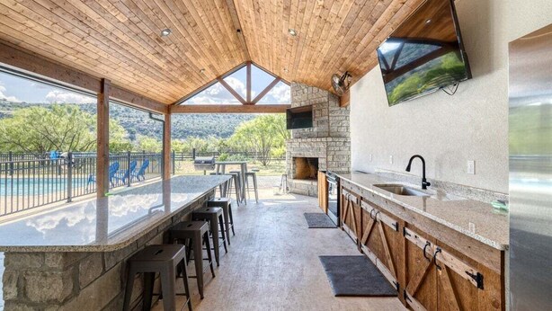 A modern kitchen with a stone backsplash, wooden ceiling, and a large window overlooking a scenic landscape. - River Ridge @ Frio Premier Rental Homes (Concan)