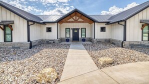 A two-story building with a symmetrical facade, a central entrance with a wooden overhang, and a gravel driveway. - River Ridge @ Frio Premier Rental Homes (Concan)