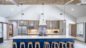 A spacious kitchen with a large island, wooden bar stools, and pendant lighting. - River Ridge @ Frio Premier Rental Homes (Concan)