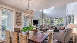 A spacious living room with a wooden dining table, wicker chairs, and a grey sofa. - GolfCourseView~6 Person GolfCart~HeatedPool*~Hot tub~FREE GOLF+Pet considered (Miramar Beach)