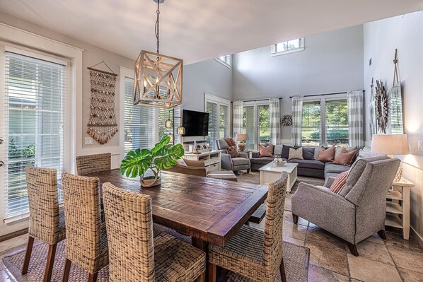A spacious living room with a wooden dining table, wicker chairs, and a grey sofa.
