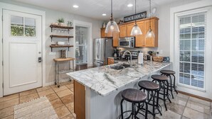 A modern kitchen with a marble island, wooden bar stools, and pendant lighting. - GolfCourseView~6 Person GolfCart~HeatedPool*~Hot tub~FREE GOLF+Pet considered (Miramar Beach)