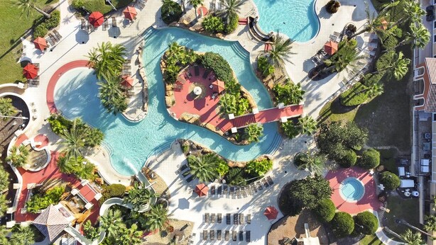 An aerial view of a resort with multiple swimming pools, sun loungers, and palm trees. - 4BR Regal Palms | Lazy River, Slide + Arcade (Davenport)