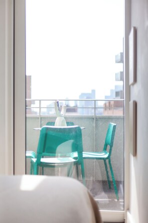 Ein Balkon mit zwei grünen Stühlen und einem weißen Tisch mit Blick auf eine Stadtlandschaft.