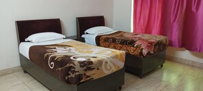 Two single beds with headboards, a small table, and a chair in a room with a wooden floor and a window with pink curtains. - Hotel Galaxy Intercontinental (Gaya)