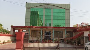 A hotel with a large green glass facade, a covered entrance with a red roof, and a white van parked in front. - Hotel Galaxy Intercontinental (Gaya)