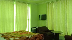 A hotel room with a bed, two armchairs, a small table, a ceiling fan, and a TV mounted on the wall. - Hotel Galaxy Intercontinental (Gaya)