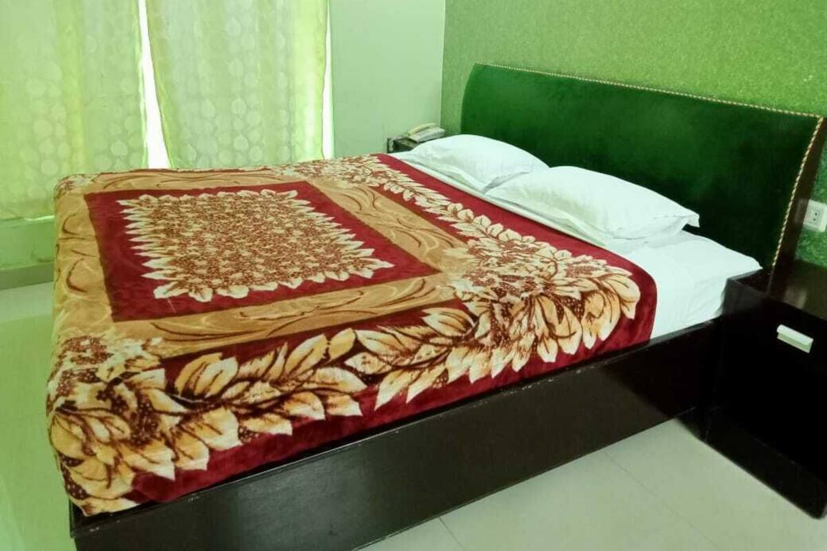 A bed with a floral bedspread, a green upholstered headboard, and white pillows.