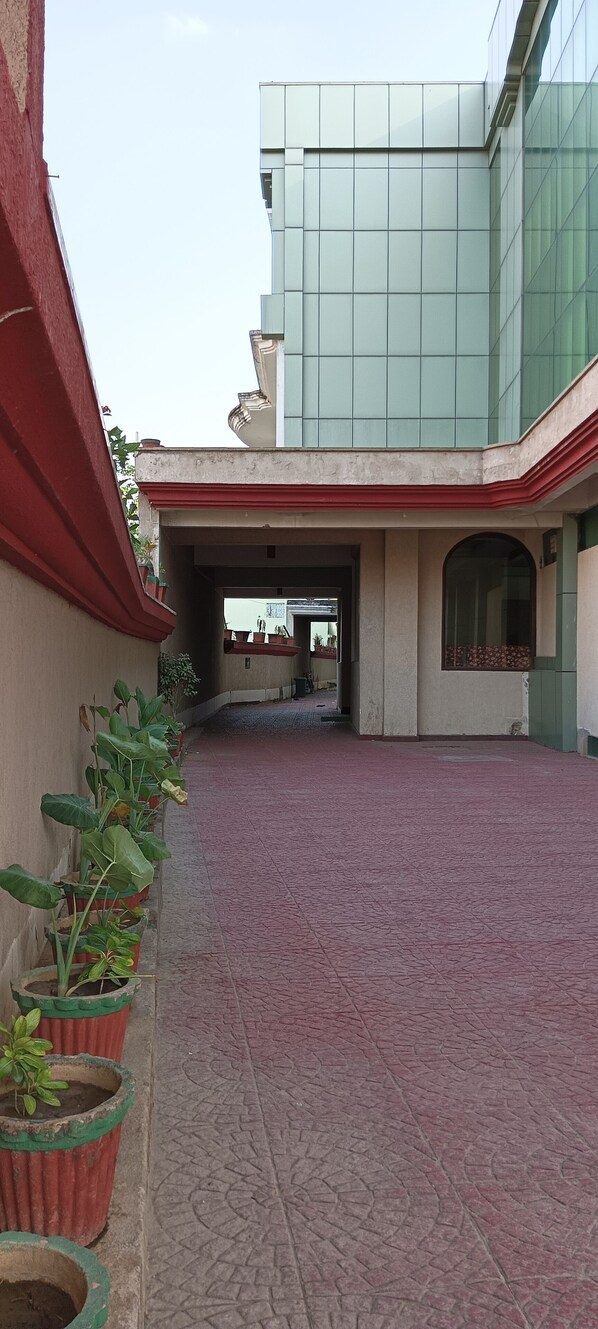 A covered walkway with potted plants, leading to a building with a modern glass facade. - Hotel Galaxy Intercontinental (Gaya)