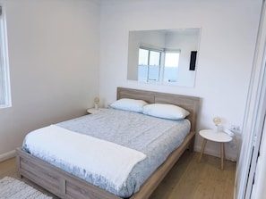 Quarto com cama de madeira, mesa de cabeceira, uma mesinha redonda e um espelho na parede.