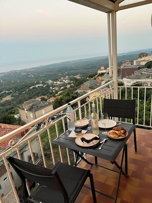 A balcony with a table set for two, overlooking a scenic landscape.