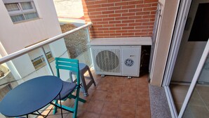 A balcony with a table and chairs, a brick wall, and an air conditioning unit. - Apartamento Vacacional con Piscina y Garaje (Torreblanca)