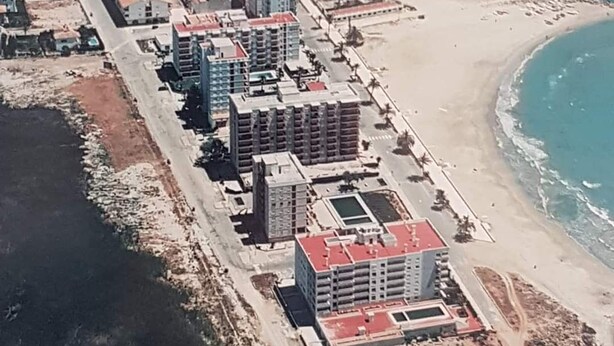 An aerial view of a coastal hotel with multiple buildings, a sandy beach, and a curved coastline. - Apartamento Vacacional con Piscina y Garaje (Torreblanca)