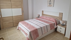 A bedroom with a bed, bedside tables, a wardrobe, and a wall-mounted artwork. - Apartamento Vacacional con Piscina y Garaje (Torreblanca)
