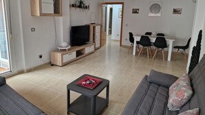 A modern living room with a TV, sofa, and dining area. - Apartamento Vacacional con Piscina y Garaje (Torreblanca)