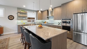Una cocina moderna con una isla central, electrodomésticos de acero inoxidable, armarios de madera e iluminación colgante.