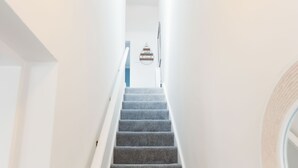 Eine schmale Treppe mit weißen Wänden und grauen Teppichstufen führt zu einer Tür oben.