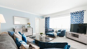 Ein modernes Wohnzimmer mit einer Couch, Sesseln, einem Couchtisch und einem Fernseher.