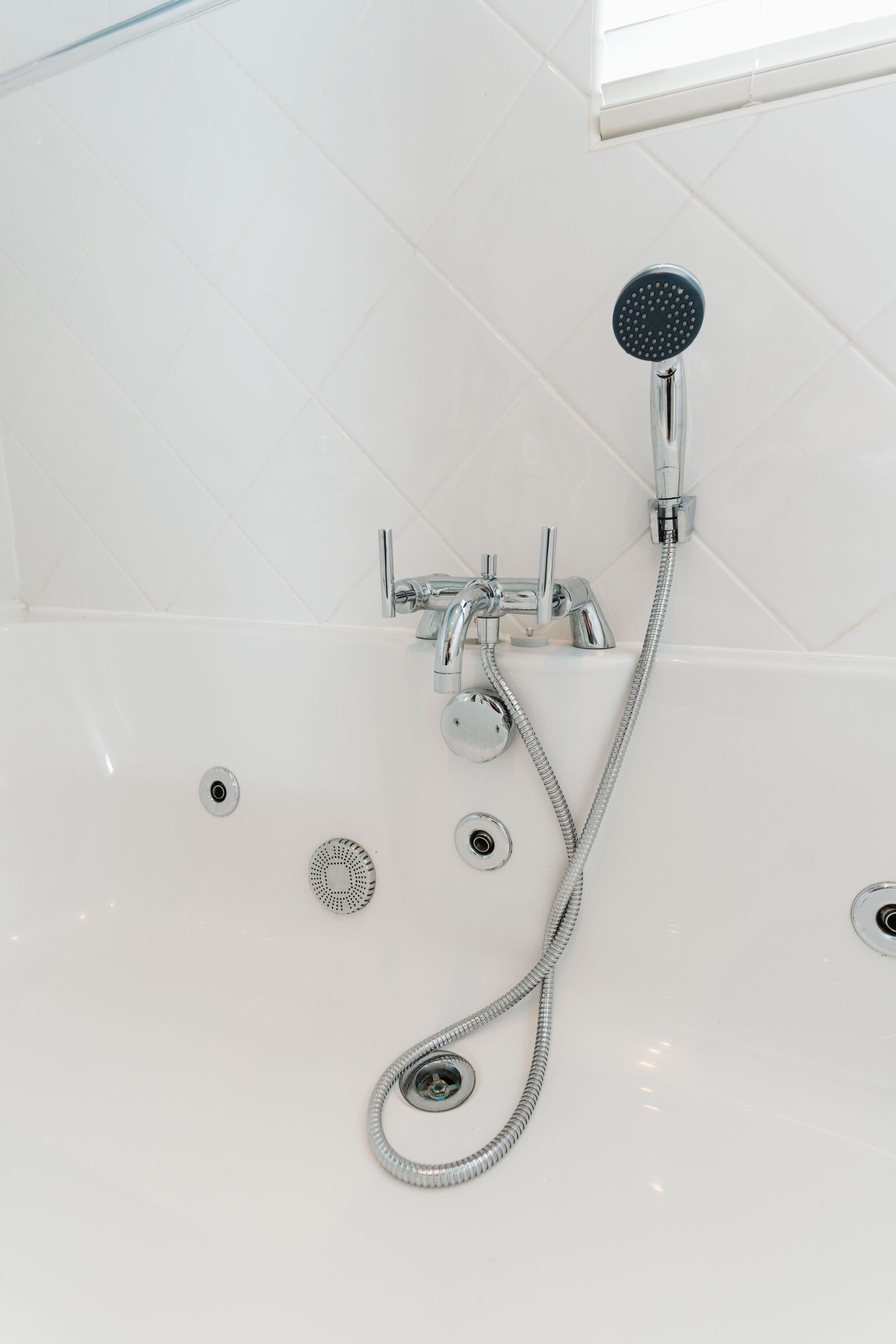 A modern bathroom with a bathtub, a handheld showerhead, and a built-in faucet.