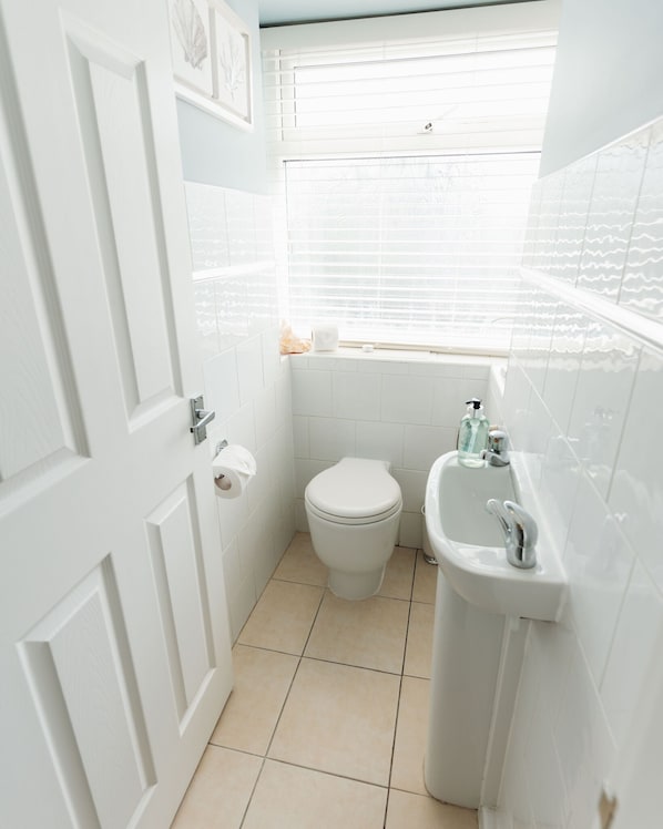 Un baño pequeño y blanco con inodoro, lavamanos y ventana.