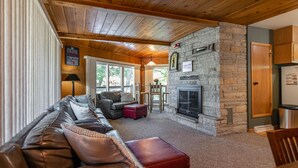 A cozy living room with a stone fireplace, leather sofa, and a dining area with a table and chairs.